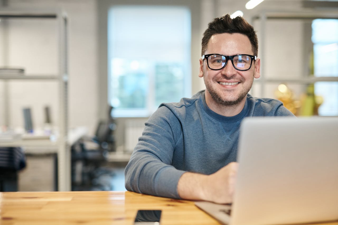 gallery-06 Happy man wearing glasses working remotely on laptop in modern office environment.